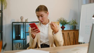 Businesswoman programmer software developer in suit working, making online purchase payment shopping with credit bank card and smartphone at modern office desk with laptop. Freelancer business woman