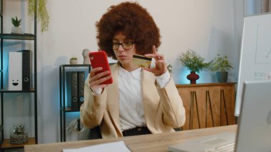 Businesswoman programmer software developer working, making online purchase payment shopping with credit bank card and smartphone at modern office desk with laptop. Female freelancer business woman