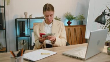 Rich business woman working on smartphone counting money cash, calculate earnings income profit at office workplace. Professional manager freelancer girl. Business people. Employment, occupation