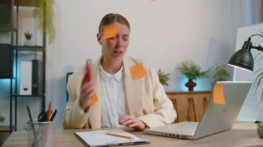 Tired exhausted businesswoman in suit working on laptop at office with many sticker task inscriptions. Freelancer woman busy occupation feels sad boredom overworked multitasking. Panic attack deadline