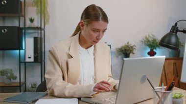 Businesswoman in suit working on laptop computer smiling friendly at camera and waving hands gesturing hello, hi, greeting or goodbye, welcoming with hospitable expression at office workplace desk
