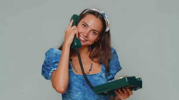 Hey you, call me back. Pretty young woman in princess dress talking on wired vintage telephone of 80s, says hey you call me back. Adult stylish female girl isolated on gray studio background indoor