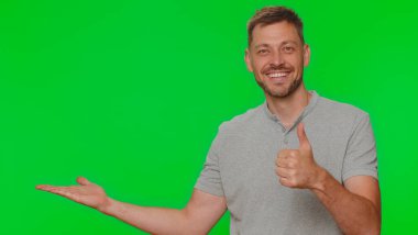 Sakallı yakışıklı genç adam, başparmağını kaldırıyor ve sol boş yeri işaret ediyor. Ticari metinler için reklam alanı, ürün tanıtımı için kopya alanı. Yetişkin adam krom anahtar stüdyo arka planında izole