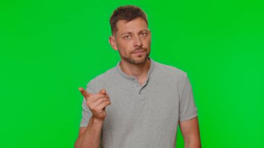 Üzgün genç adam parmağını sıkar ve hayır der, dikkatli ol, azarla ve tehlike hatasını önlemek için tavsiye ver, onaylanmama işareti. Yeşil krom anahtar arka planında izole edilmiş yetişkin tarzı bir adam.