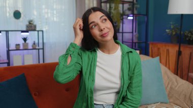 I dont know what to say. Confused girl feeling embarrassed about ambiguous question, having doubts, no idea, being clueless and uncertain. Young attractive woman at home living room on orange couch