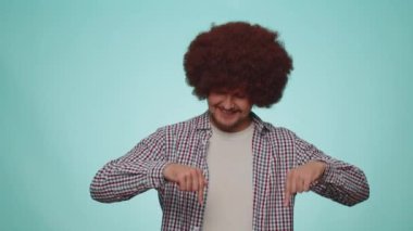 Look at advertisement. Man pointing down, saying to subscribe, gesturing ok and like, showing place for commercial, promotional information below. Young guy isolated on blue studio wall background