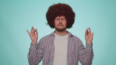 Keep calm down, relax, inner balance. Man breathes deeply with mudra gesture, eyes closed, meditating with concentrated thoughts, peaceful mind. Young adult guy isolated on blue studio wall background