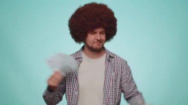 Happy bearded man holding fan of cash money dollar banknotes celebrate dance, success business career, lottery game winner, big income, wealth. Young adult guy boy isolated on blue studio background