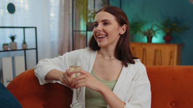 Happy caucasian girl hold glass of champagne cheering drinking, celebrate success win, career grow up, lucky situation at home in living room. Young woman celebrating rent or purchase of new house
