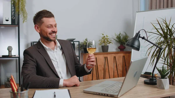Businessman working on laptop celebrate successful contract agreement with colleague client at office workplace desk. Freelancer man drinking champagne. Online remote video call conversation job