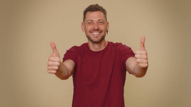 Like. Bearded handsome young man raises thumbs up agrees with something or gives positive reply recommends advertisement likes good. Adult stylish guy isolated alone on beige studio background indoors