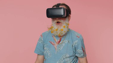 Exited elderly stylish man use virtual reality futuristic technology VR app headset helmet to play simulation 3D 360 video game, drawing. Grandfather on pink studio background. People sincere emotions