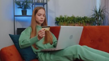 Portrait of caucasian girl using credit bank card and laptop computer while transferring money, purchases online shopping, order food delivery at home. Young child kid sit on couch at home living room