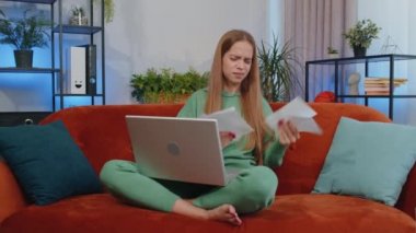 Stressed girl at home room looking at unpaid bank debt bills, doing paperwork, planning budget, calculate finances mortgage payments. Displeased young child kid throws paper bills sitting on couch