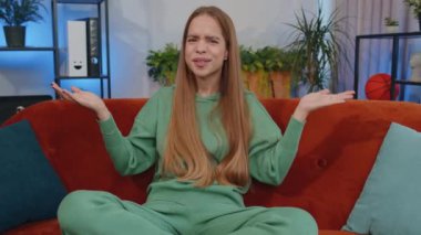 What. Why. Lovely girl raising hands in indignant expression, asking reason of failure, demonstrating disbelief irritation by troubles at home apartment. Young child kid in room sitting on orange sofa
