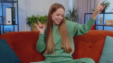 Overjoyed delighted caucasian girl showing rock n roll gesture by hands, cool sign, shouting yeah with crazy expression, dancing, emotionally rejoicing in success. Young child kid at home apartment