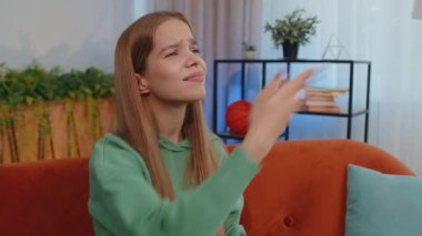 Please, God help. Girl praying sincerely with folded arms, looking upward and making wish, asking with hopeful imploring expression, begging apology. Young child kid sit on couch at home living room
