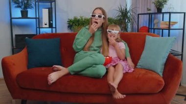 Girls friends siblings watching favorite tv show movie and eating popcorn, sitting on sofa. Female children kids family having fun laughing, relaxing, watch television online stream at home on couch