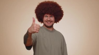 Like. Bearded adult man with lush coiffure raises thumbs up agrees with something or gives positive reply recommends advertisement likes good. Young guy isolated alone on beige studio background
