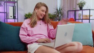 Portrait of caucasian girl sitting on couch, looking at camera, making video webcam conference call with friends or family, enjoying pleasant conversation. Young woman laughing, waving hello at home