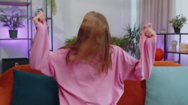 Overjoyed delighted caucasian adult girl showing rock n roll gesture by hands, cool sign, shouting yeah with crazy expression, dancing, emotionally rejoicing in success. Young woman at home apartment