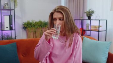 Portrait of thirsty lovely girl sitting indoors holding glass of natural aqua make sips drinking still water preventing dehydration. Woman with good life habits, healthy slimming, weight loss concept