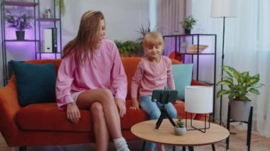 Blogger mother and child kid daughter sit at home living room enjoy listening music, dancing, recording video content for social media. Family enjoy selfie filming by internet network wifi connection