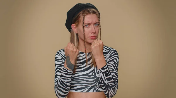 Aggressive angry pretty young woman in crop top trying to fight at camera, shaking fist, boxing with expression, punishment. Adult stylish female girl isolated alone on beige studio background indoors