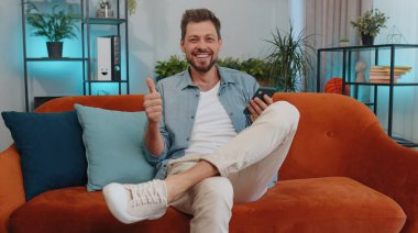 Portrait of man use mobile smartphone typing browsing say Wow yes found out great big win good news celebrate lottery jackpot doing winner gesture. Young guy at home in living room sitting on sofa