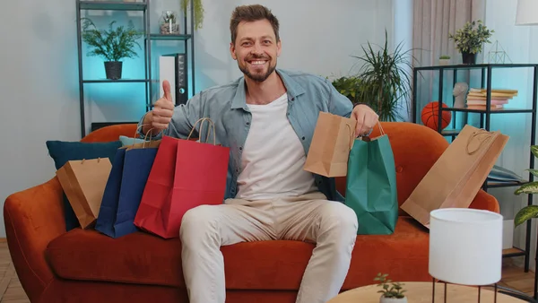 Portrait of caucasian adult man happy shopaholic consumer came back home after shopping sale with bags. Young guy satisfied received parcels from online order at modern home apartment living room
