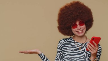 Pretty young female girl using smartphone pointing left empty place, advertising area for commercial text, copy space for goods promotion, positive feedback, recommends wifi cellular connection 5G