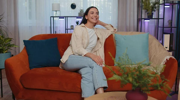 Portrait of happy calm girl in shirt smiling friendly, glad expression looking away dreaming resting, relaxation feel satisfied concept good news. Young caucasian woman sitting on sofa at home room