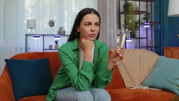 Sad young woman looks pensive of unrequited love, suffers from unfair situation, drinking champagne. Problem, break up, depressed feeling bad annoyed, burnout, bankruptcy. Girl sitting at home room
