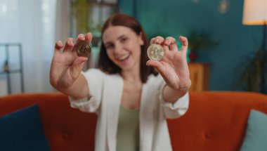 Girl freelancer hold two gold BTC coins at home successful developer programmer. Woman stock trader earning bitcoins after online monitoring trading operations. Increasing wealth, financial prosperity