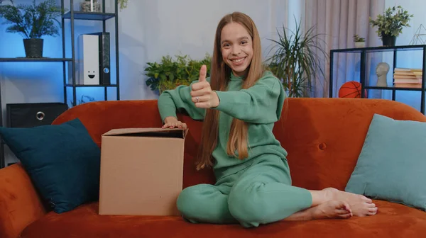 Portrait of happy girl unpacking delivery parcel sitting at home. Smiling satisfied young child kid shopper, online shop customer opening cardboard box receiving purchase gift by fast postal shipping