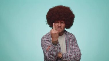 Aggressive crazy hooligan man showing around his middle finger, demonstrating protest with impolite rude gesture of disrespect, rejecting communication. Young adult guy isolated on blue background