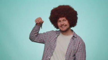 Handsome bearded man real estate agent lifting hand showing the keys of new home house apartment, buying or renting property, mortgage loan. Young adult guy boy isolated on blue studio background