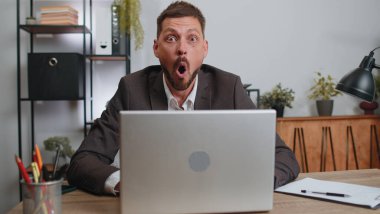 Businessman hiding behind laptop computer, making funny face, fooling around, putting his tongue out remote working disrespecting someone at home office. Male freelancer business man busy occupation