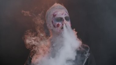 Kanlı suratlı ürkütücü adam, Cadılar Bayramı stili zombi makyajı. Korkunç yaralı ölümsüz adam burnundan ve ağzından duman üflüyor, korkunç bir şekilde gülümsüyor. Voodoo ayinleri. Tematik parti. Şeytani canavar, canavar.
