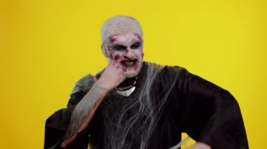 Sahte yara izleriyle makyaj yapan zombi adam başarıyı kutluyor. Çığlık atarak seviniyor. Sarı stüdyo duvarına 