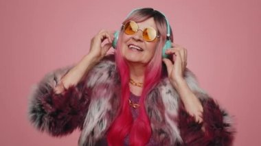 70 'lerde müzik dinleyen komik yaşlı bir kadın disko partisinde dans ederken gülümseyen ellerini ritmik bir şekilde hareket ettiren, eğlenen. Büyük anne zaferi kutluyor, doğum günü pembe duvar arkasında izole edilmiş.