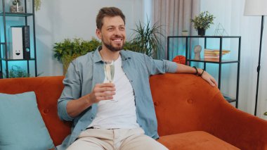 Neşeli beyaz bir adam elinde şampanya kadehiyle içki içiyor, başarıyı kutluyor, kariyer sahibi oluyor, evinde şanslı bir durumda. Kirayı veya yeni evi satın almayı kutlayan genç adam.