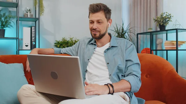 Portrait of caucasian man sitting on couch, looking at camera, making video webcam conference call with friends or family, enjoying pleasant conversation. Young guy laughing, waving hello at home