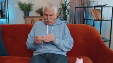 Zavallı yaşlı büyükbaba, elinde kumbarası ve bir dolarlık banknotla, yetersiz miktarda para tutuyor. Finansal kriz. İflas. Yoksulluk ve yoksulluk. Oturma odasındaki kanepede oturan yaşlı adam.