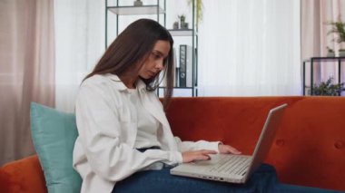 Portrait of girl sitting on couch closing laptop pc after finishing work in living room at home. Young woman freelancer working online, remote job. E-learning, browsing internet on notebook computer