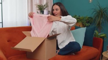 Portrait of happy girl unpacking delivery parcel sitting at home. Smiling satisfied young woman shopper, online shop customer opening cardboard box receiving purchase gift by fast postal shipping