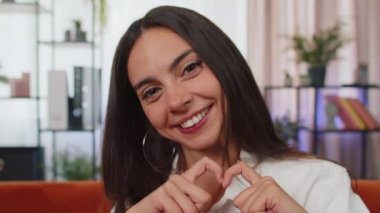 Ben de seni seviyorum. Yetişkin bir kız aşkın sembolünü yapar, kameraya kalp işaretini gösterir, romantik duyguları ifade eder, samimi olumlu duyguları ifade eder. Sadaka, minnettarlık, bağış. Genç bayan, yakın plan mutlu yüz.
