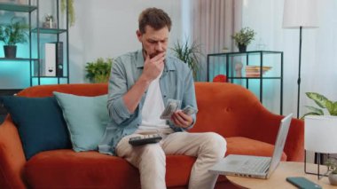 Planlama bütçesi. Zengin ve mutlu bir adam nakit sayıyor hesap makinesi kullanıyor ve evdeki faturaları hesaplıyor. Gelir getiren, kazanan, planlı tatil için para biriktiren, hediyeler alan neşeli genç adam.
