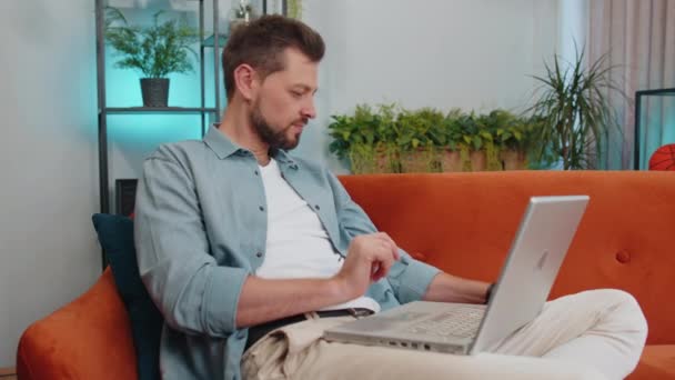 白人男子在汇款 购买网上购物 在家里订购食品时使用信用卡和手提电脑的肖像 小伙子坐在家里客厅的沙发上 — 图库视频影像