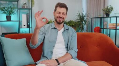 - Tamam. Mutlu, neşeli, yakışıklı bir adam kameraya bakıp, olumlu bir hareket gösteriyor, işaret gibi, oturma odasında turuncu koltukta oturan güzel bir şeyi onaylıyor. Modern ev dairesindeki genç adam.